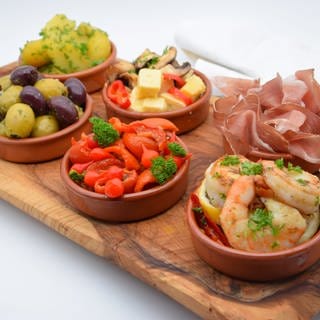 Auf einem Brett stehen sechs Schälchen mit verschiedenen spanischen Tapas: Oliven, Garnelen, Kartoffeln, Schinken, Paprika. Ob Garnelen, Oliven, Kartoffeln, getrocknete Tomaten ... die Möglichkeiten für Tapas sind grenzenlos. SWR1 Pfännle-Koch Eberhard Braun liefert euch Tapas-Inspirationen.