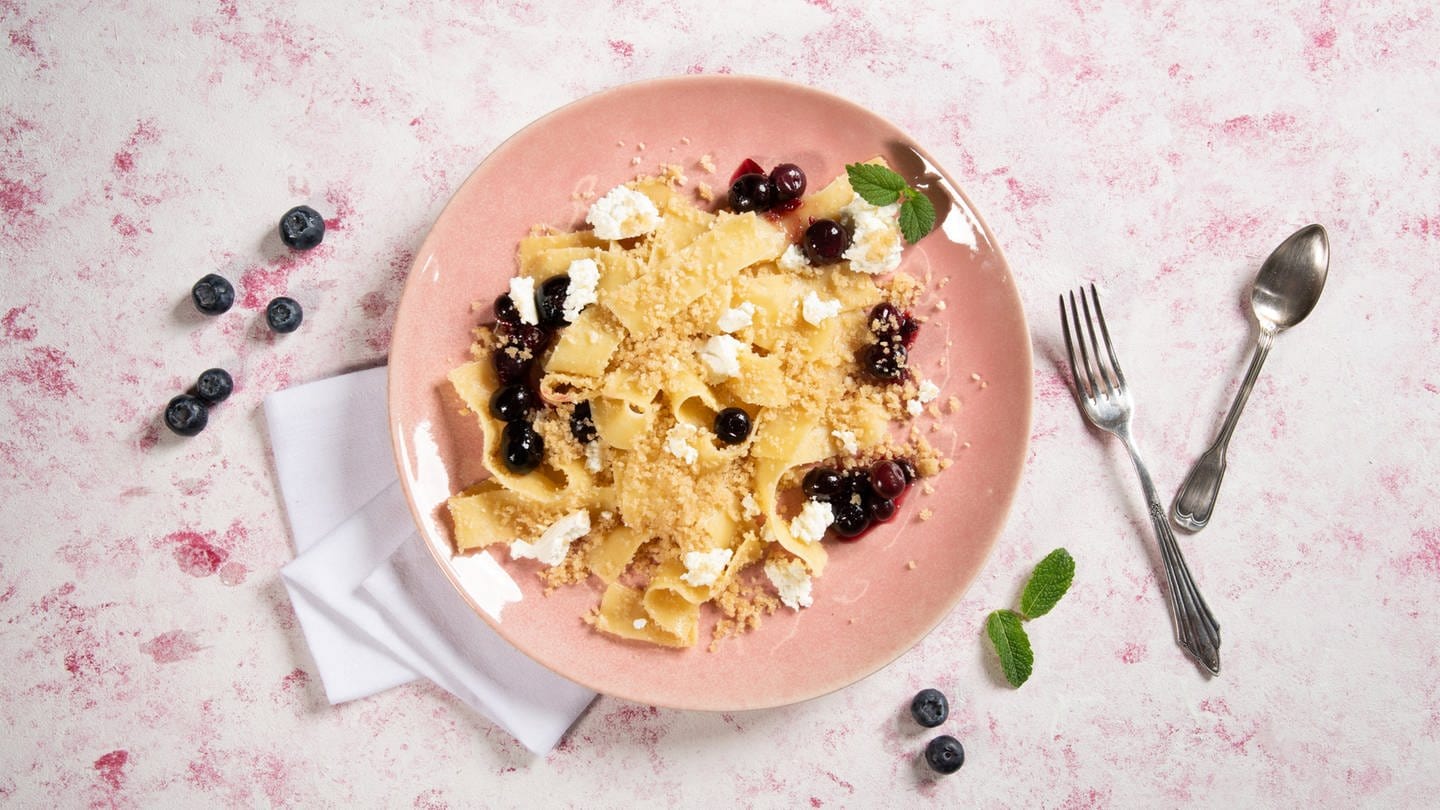 Auf einem Teller angerichtet: Eine süße Pasta-Variante aus Bandnudeln, mit Schichtkäse und Blaubeerkompott.