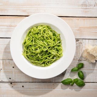 Grünes Pesto auf Spaghetti in einem Teller angerichtet.