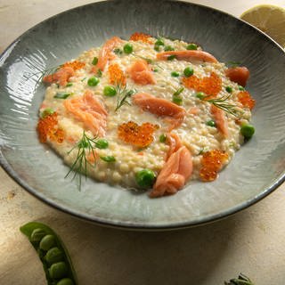 Riebele Risotto mit gerupfter Lachsforelle und Kaviar auf einem Teller angerichtet.