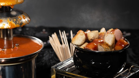 Von einem Currywurst Brunnen läuft Currywurstsauce und eine Schale mit Currywurst steht daneben.