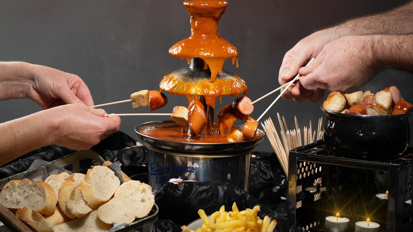 Von einem Currywurst Brunnen läuft Currywurstsauce und einge Menschen halten ihre Currywurst in die Sauce.