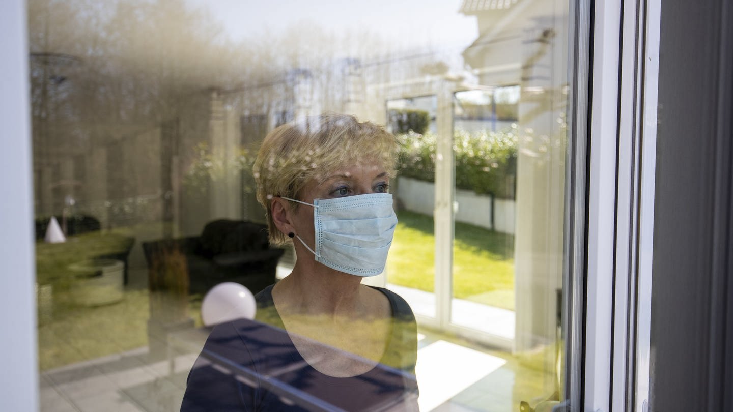 Covid - 19: häusliche Quarantäne Person schaut durch die Scheibe nach draußen mit Mundschutz