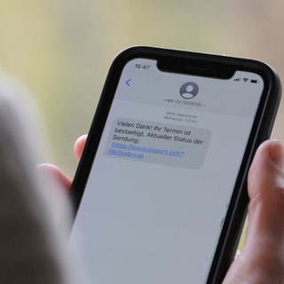 Eine Frau hält ein Smartphone in ihrer Hand, auf dessen Display eine Betrugs-SMS zu lesen ist. Beim sogenannten Smishing setzen Kriminelle darauf, dass Verbraucher auf den mitgeschickten Link klicken und sich in einem nächsten Schritt unwissentlich eine Schadsoftware runterladen.