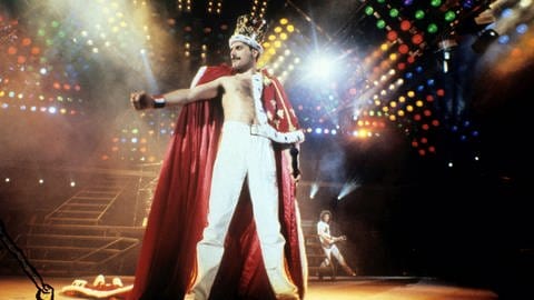 Freddie Mercury von der Band Queen auf der Bühne mit einer Krone und Umhang an