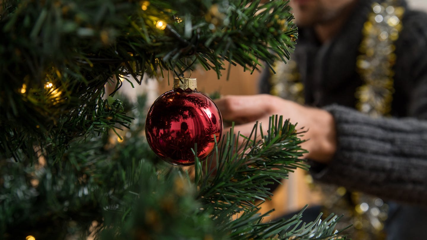 Ein Mann schmückt einen Weihnachtsbaum.