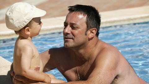 Vater spielt mit Baby an einem Pool | So bleiben Sie bei über 30 Grad cool
