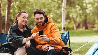 Camper sitzen vor Smartphone | So kommen Sie im Urlaub sorglos mobil ins Internet
