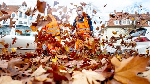 Zwei städtische Mitarbeiterinnen befreien einen Radweg mit Laubbläsern vom Herbstlaub. | Wer muss Herbstlaub beseitigen?