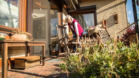 Eine Frau klappt ihre Gartenmöbel ein und stellt sie über den Herbst und Winter zurück ins Haus. Zeitumstellung | Winterzeit 