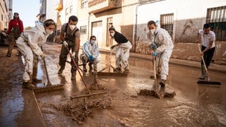 Helfer beseiteiten den Schlamm von den Straßen in Valencia nach der Flut. (Symbolbild). Fluthelfer Nico Vogel hilft mit seinem Geländewagen vor Ort.