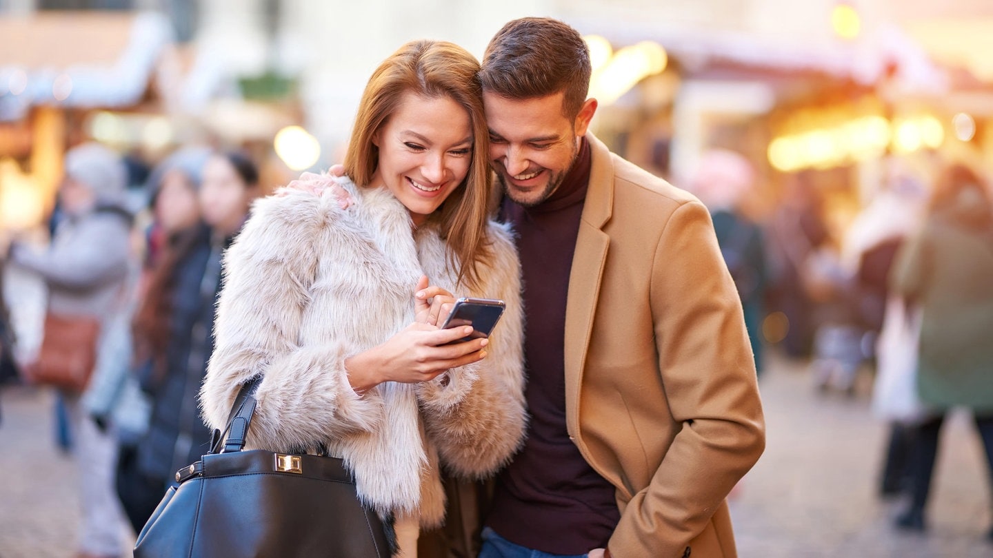 Ein Paar auf dem Weihnachtsmarkt schaut auf ein Smartphone.