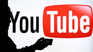 Person mit Smartphone vor YouTube Logo