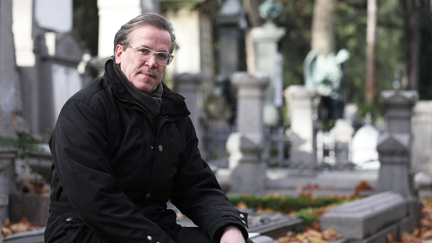 Christoph Kuckelkorn, Bestattungsunternehmer und Karnevalspräsident, sitzt auf dem Melatenfriedhof an Gräbern.
