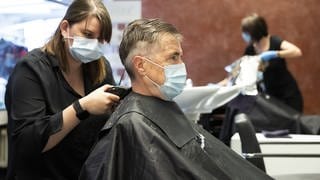 Eine Friseurin schneidet einem Kunden mit Schutzausrüstung die Haare