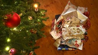 Zerknülltes Geschenkpapier liegt neben einem Weihnachtsbaum auf dem Boden