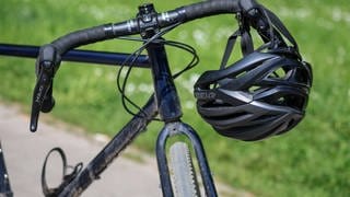 Ein Fahrradhelm hängt an einem Fahrradlenker | Darauf sollten Sie beim Kauf von Fahrradhelmen achten