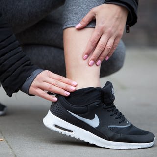 Sportverletzung beim Laufen: Eine Frau fasst sich an ihren schmerzenden Knöchel | So schützen Sie sich als Anfänger vor Sportverletzungen