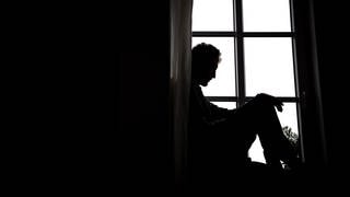 Mann sitzt traurig im Fensterrahmen