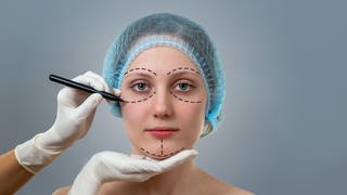 Schönheitschirurg zeichnet vor der Behandlung Linien auf dem Gesicht einer Frau