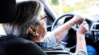 Eine über 90-jährige Frau sitzt hinter dem Lenkrad eines Autos.