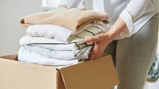 Frau packt Kleidung in Umzugskarton für Umzug oder Kleiderspende