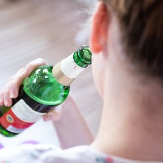 Alkoholsucht bei Jugendlichen: Ein Mädchen wurde von hinten fotografiert, wie sie aus einer Bierflasche trinkt 