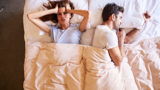 Eine Frau liegt neben einem Mann im Bett und kann nicht schlafen
