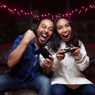 Ein Mann und eine Frau sitzen auf einer Couch und spielen Videospiele.