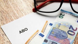 Abo als Weihnachtsgeschenk: Ein weißer Brief mit Überschrift Abo neben einer Brille und Euro Geldscheinen
