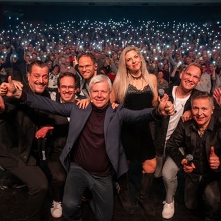 Ein unvergesslicher Abend! Die Band "Pop History" und SWR1 Musikchef Bernd Rosinus posieren für ein Abschiedsfoto vor der leuchtenden Menge.