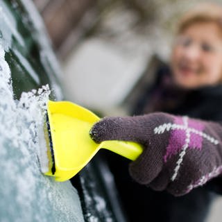 Eine Frau kratzt am Eis von einer Autoscheibe