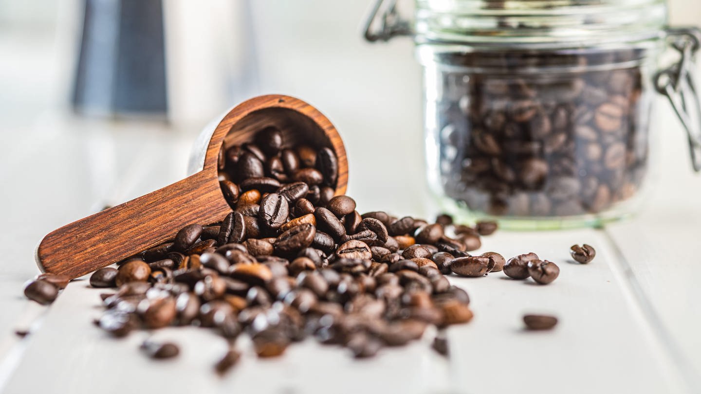 Geröstete Kaffeebohnen fallen aus einem Holzlöffel | Wie gesund ist Kaffee wirklich?
