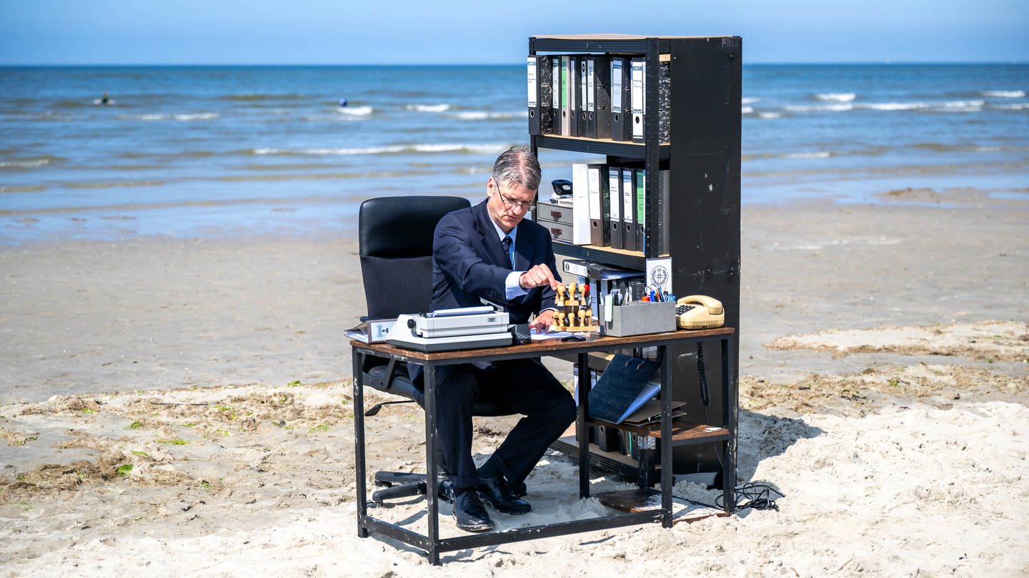 Workation – Ein Mann sitzt am Strand am Schreibtisch