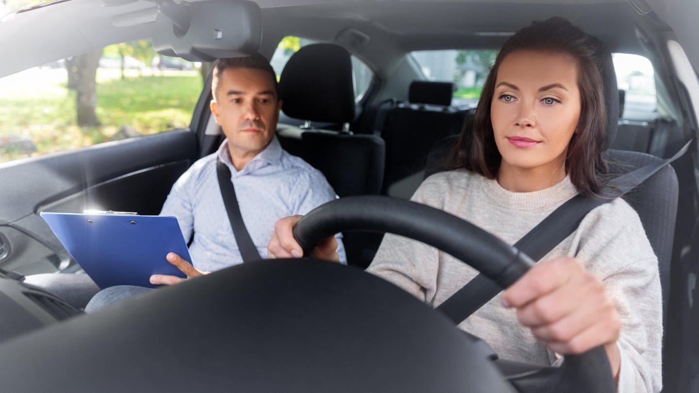 Eine junge Frau macht eine Fahrstunde mit ihrem Fahrlehrer | Warum ist der Führerschein heutzutage so teuer?