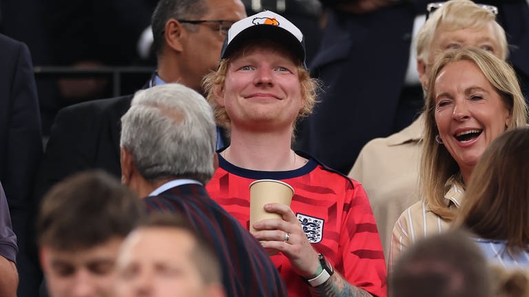 11. Juli: Er hat es wieder getan! Ed Sheeran ist erneut im Stadion Dortmund gesichtet worden, um sein Team zu unterstützen. Als England in der 90. Minute das entscheidende Tor macht, war Schluss mit entspanntem Kaffee trinken (s. Foto). Der Musiker sprang auf und jubelte auf der Tribüne. Unter die Zuschauer mischte sich auch noch ein anderer Superstar: Adele.