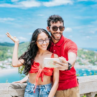 Ein Pärchen auf einer Aussichtsplattform im Urlaub macht ein Selfie | Digitale Urlaubsgrüße: Mit diesen Apps könnt ihr digitale Postkarten verschicken