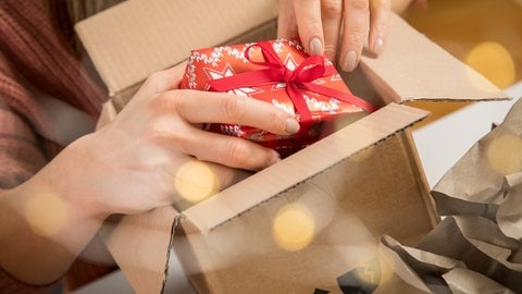 Eine Frau packt ein Weihnachtsgeschenk in ein Paket | So kommen Geschenke rechtzeitig an: Versandfristen für Weihnachtspakete und Briefe im Überblick