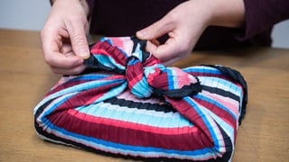 Eine Frau wickelt ein Geschenk mit der japanischen Furoshiki-Technik in ein Tuch ein | Furoshiki statt Geschenkpapier: Geschenke nachhaltig verpacken