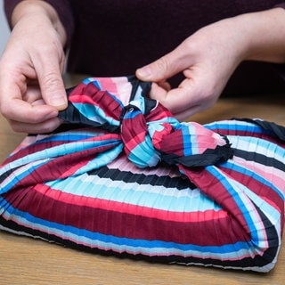 Eine Frau wickelt ein Geschenk mit der japanischen Furoshiki-Technik in ein Tuch ein | Furoshiki statt Geschenkpapier: Geschenke nachhaltig verpacken