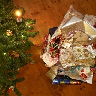 Zerknülltes Geschenkpapier liegt neben einem Weihnachtsbaum auf dem Boden | Nachhaltige Weihnachten | So reduziert ihr den Feiertagsmüll