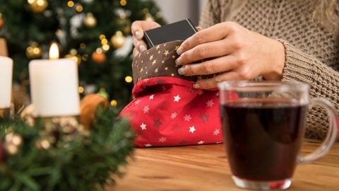 Eine Frau packt ein Weihnachtsgeschenk in einen Stoffbeutel ein. Man sieht nur ihre Hände. Der Beutel ist weihnachtlich bestickt | Nachhaltige Weihnachten | So reduziert ihr den Feiertagsmüll