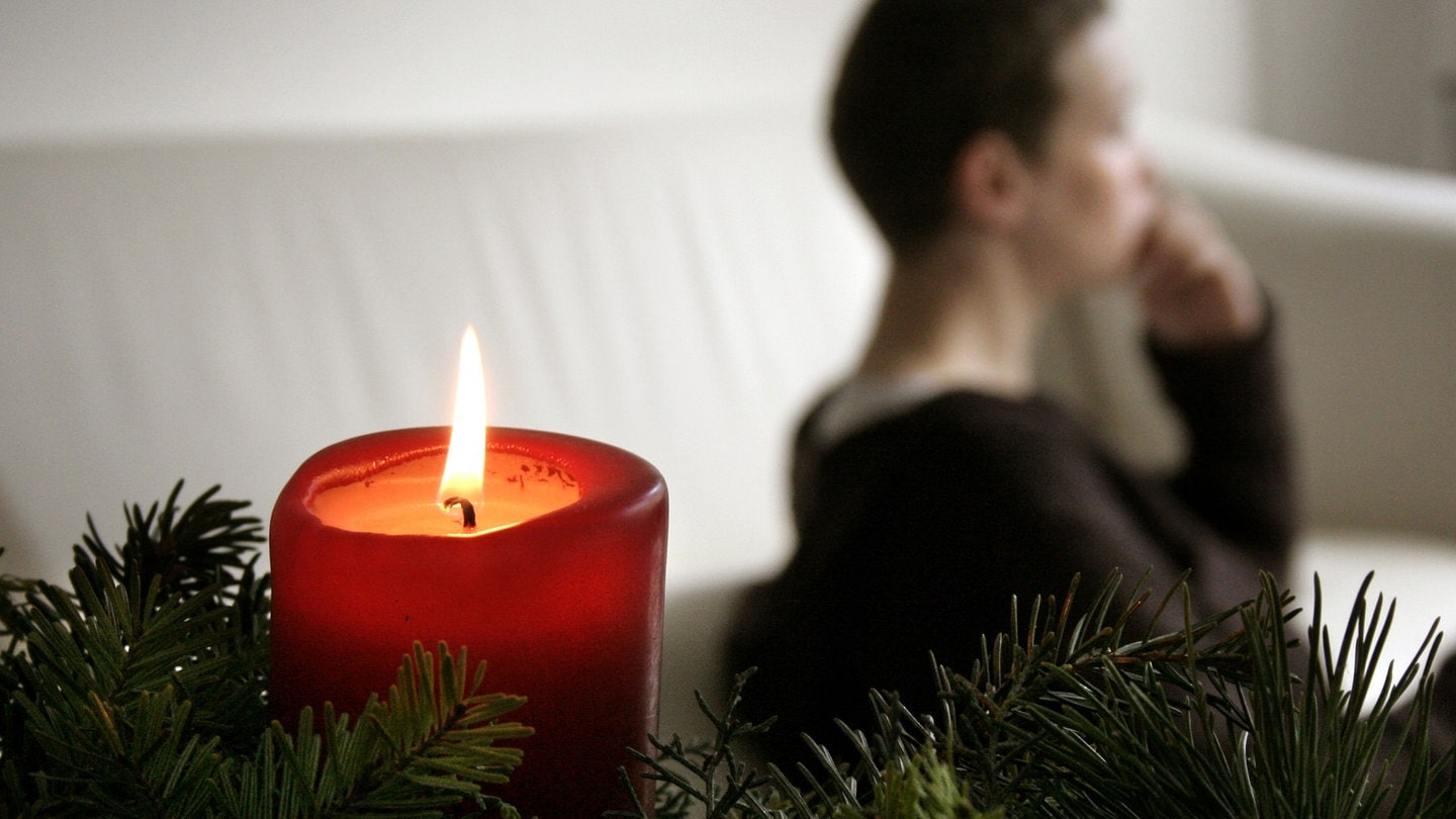 Trauer und Einsamkeit an Weihnachten: Eine nachdenkliche Frau bei Kerzenlicht. | Trauer und Einsamkeit an den Feiertagen: Wie kann man mit Einsamkeit zu Weihnachten umgehen?