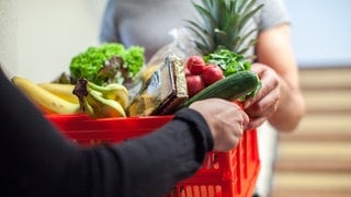 Ein Mann bringt einer jungen Frau den Einkauf vor die Wohnungstür | Darauf solltet ihr bei Lieferdiensten für Lebensmittel achten