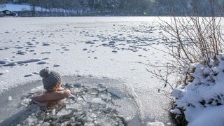 Eine Frau beim Eisbaden im Lauser Weiher bei einer gefrorenen Wasserfläche im Winter. | Schwimmen in extremer Kälte: Wie gesund ist Eisbaden wirklich?