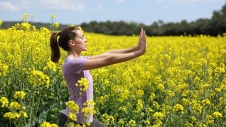 Fit mit Power Yoga, ganzheitliches Vini Yoga bei seelischen Problemen, Yoga statt Medikamente - keine Esoterik, sagt der anerkannte Yoga-Forscher Prof. Holger Cramer aus Tübingen in SWR1 Leute, sondern medizinisch anerkannte Therapie. Das Bild zeigt eine junge Frau, die Yoga Übungen in einem Feld mit gelben Blumen macht.