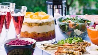 Gedeckter Tisch im Garten mit Garnelenspiessen, Rote-Bete-Dip, Spinatsalat und Trifle