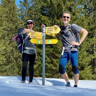 Martina und Martin Talamona stehen in Wanderoutfit an einem Wegweise. Martina hat Morbus Stargardt und ist dadurch erblindet. Trotzdem hat sie mit ihrem Mann während einer dreimonatigen Wanderung die Alpen überquert. In SWR1 Leute berichten sie von ihrer Grenzerfahrung.