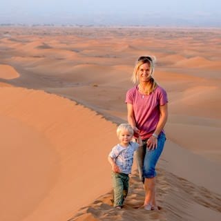 Reisejournalistin Astrid Därr steht mit ihrem Sohn auf einen Düne, im Hintergrund sieht man die Sahara-Wüste. In SWR1 Leute verrät sie, warum Reisen mit Kind kein Problem ist und wie die Reisetrends 2024 aussehen.