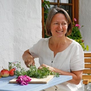 Ernährungswissenschaftlerin Karin Buchart sitzt im Garten und schneidet Kräuter. Sie erklärt in SWR1 Leute, welche Heilkräuter und Heilpflanze welche Wirkung haben und wie Naturheilkunde uns heilen kann.